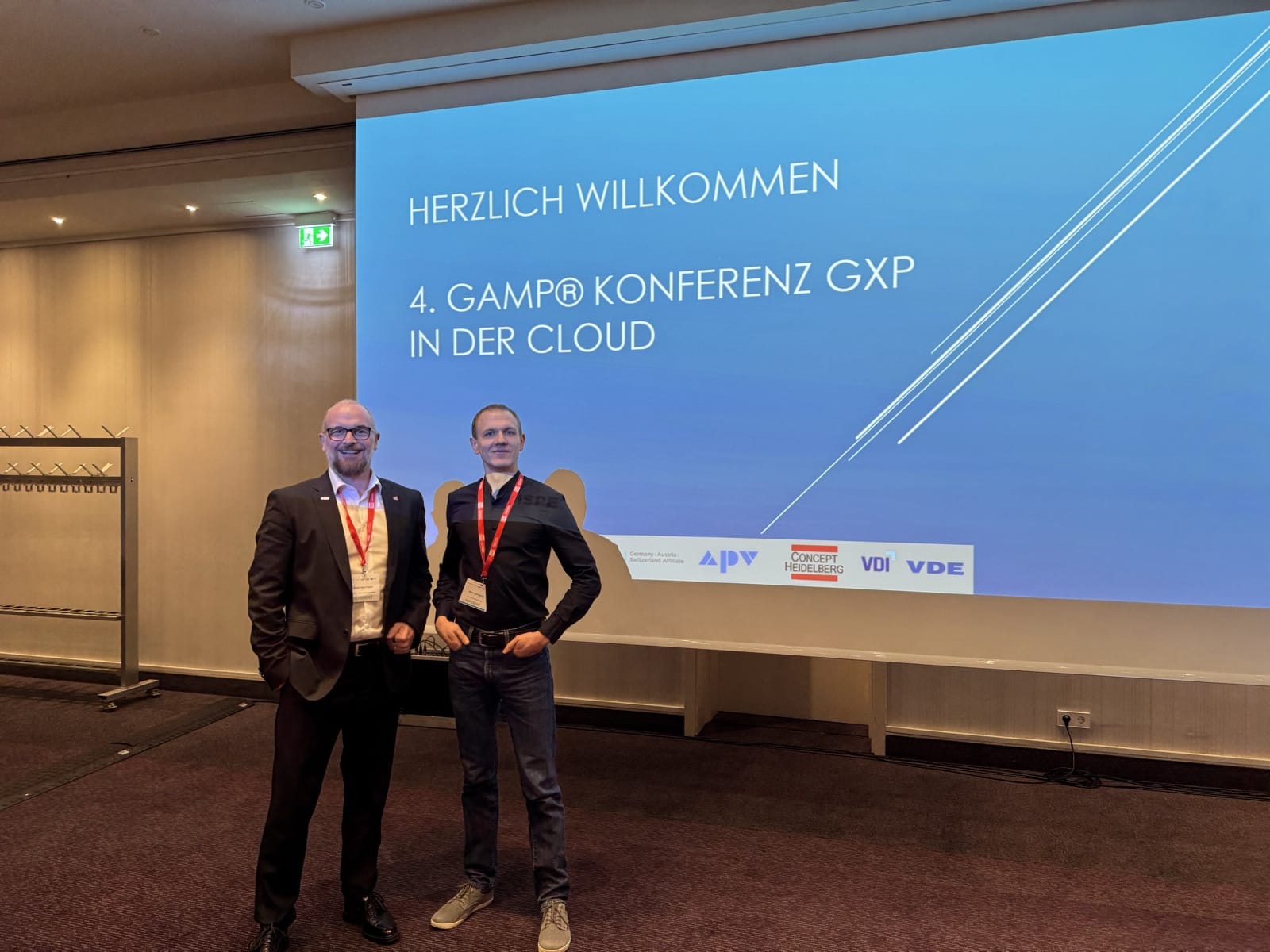 Zwei Referenten vor der Begrüßungsfolie der 4. GAMP Konferenz 'GxP in der Cloud' in Mannheim