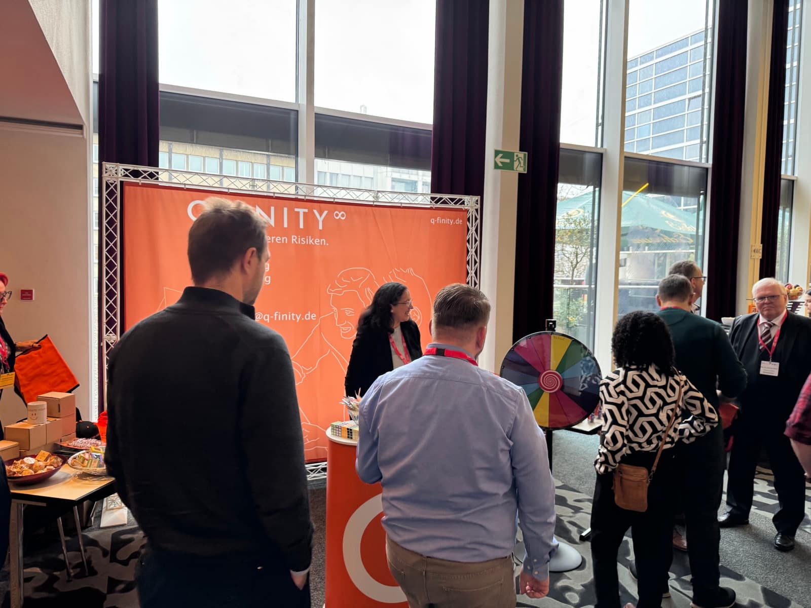 QFINITY-Messestand mit orangem Banner und Glücksrad auf der GAMP 5 Konferenz in Mannheim